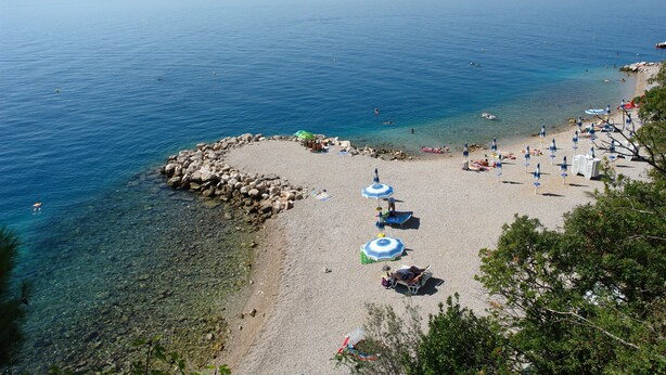A beach with clear water, rocky shore, and umbrellas. - Apartments Brankica (Dramalj)