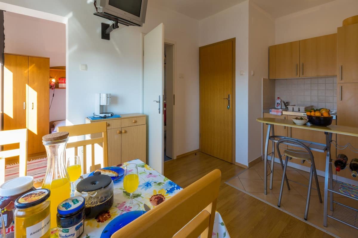 Eine kompakte Küche mit Holzausstattung, einem Esstisch mit Stühlen, einem an der Wand befestigten Fernseher und einem kleinen Kühlschrank.