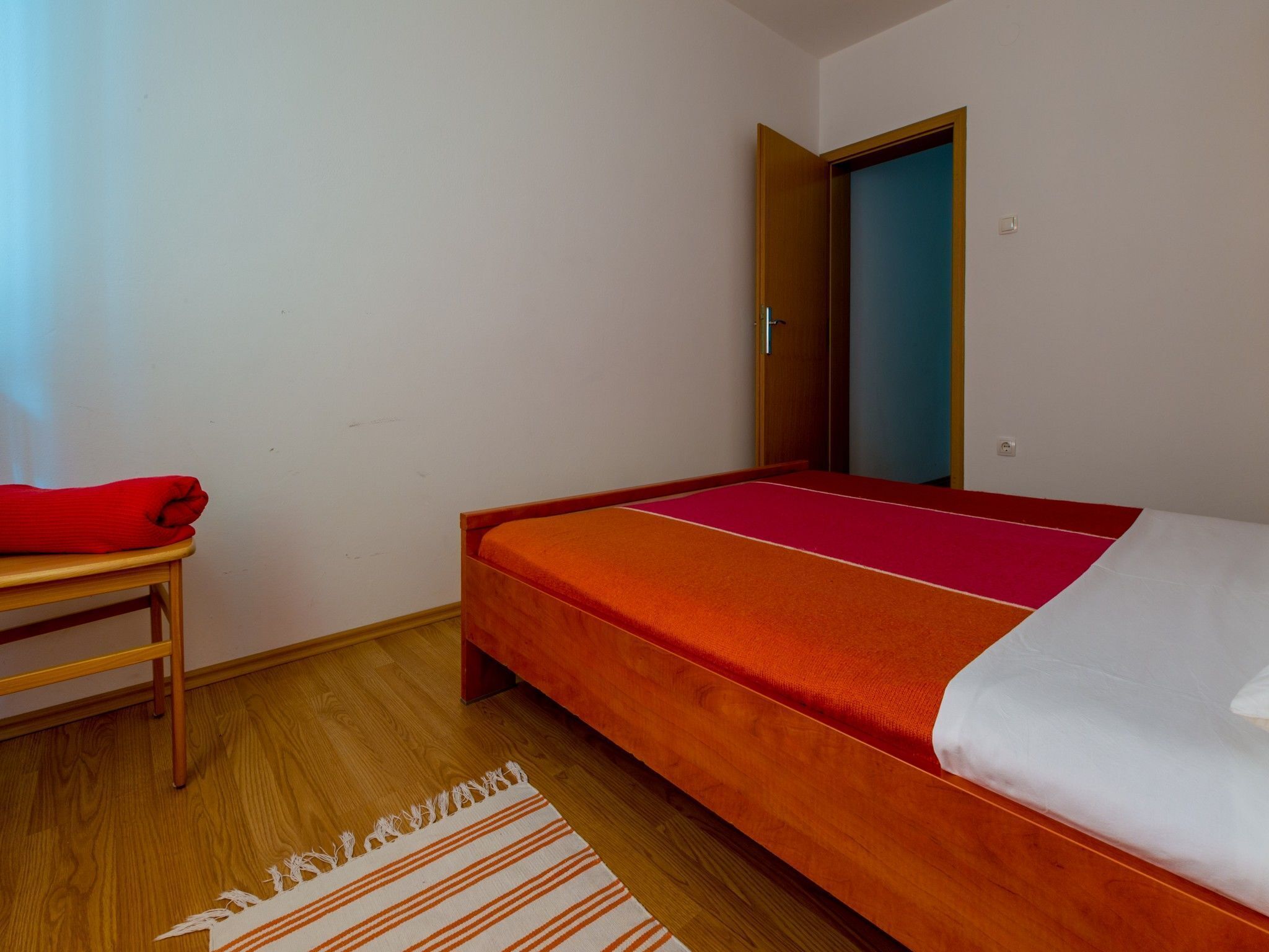 A small, neatly arranged room with a bed, a wooden table, and a door.