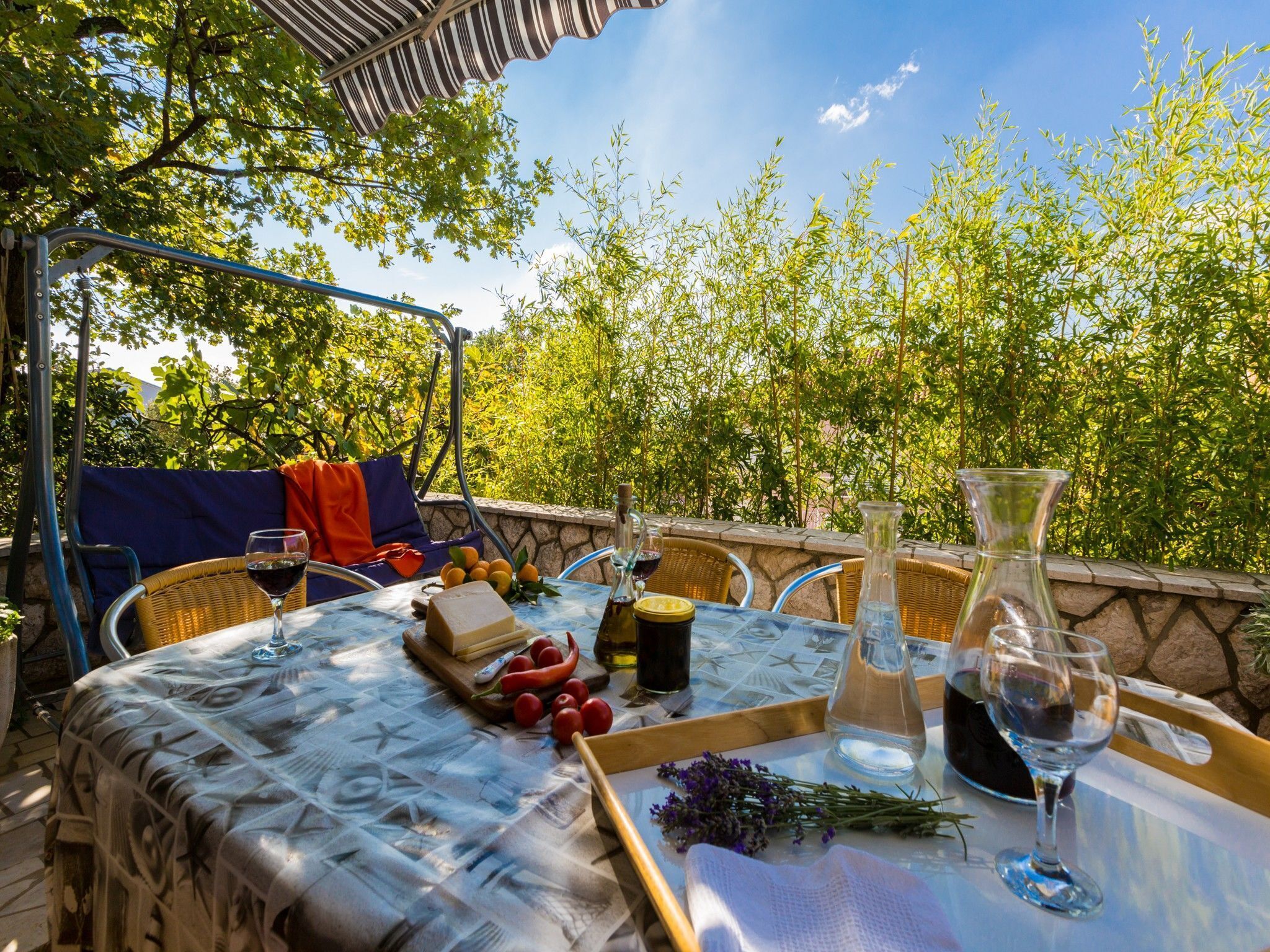 An outdoor dining area with a table set for two, surrounded by lush greenery and a clear sky.