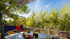 An outdoor dining area with a table set for two, surrounded by lush greenery and a clear sky. - Apartments Brankica (Dramalj)