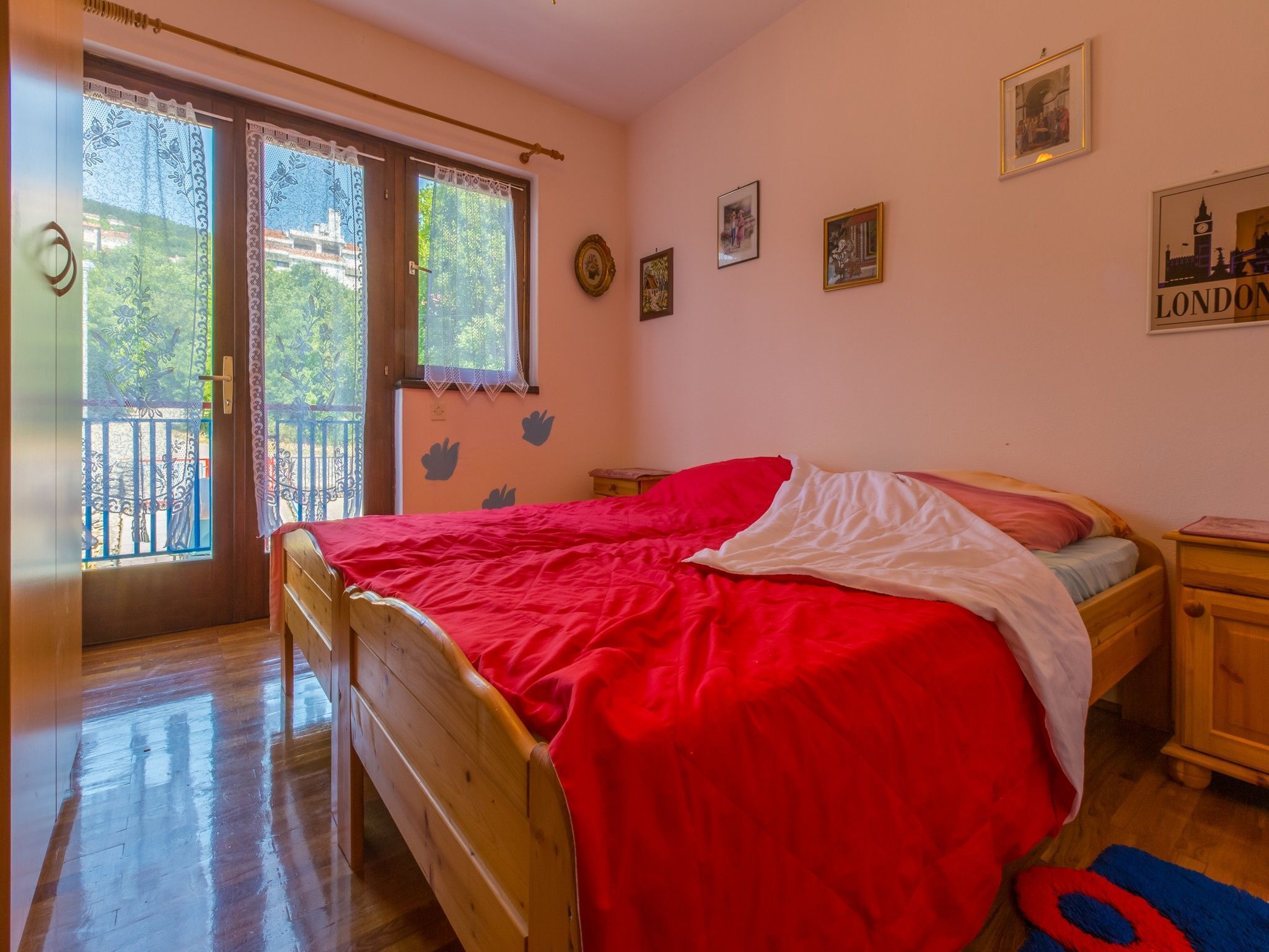 Une chambre à coucher avec un lit en bois, une couvre-lit rouge et une fenêtre ornée de rideaux en dentelle.