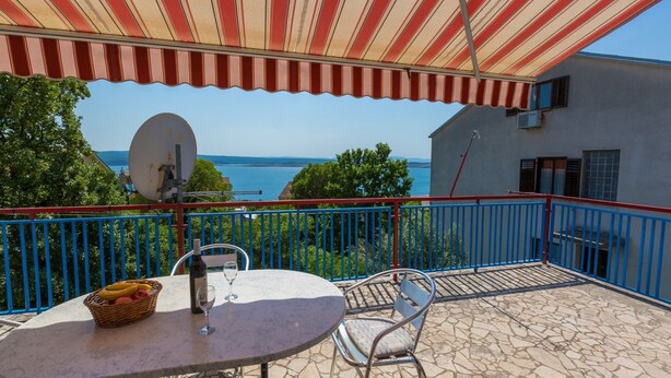 Un balcon avec une table, des chaises et un auvent rayé de rouge et de blanc. Une antenne parabolique est fixée au mur.