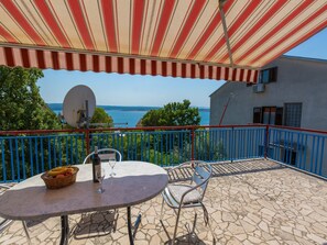Un balcon avec une table, des chaises et un auvent rayé de rouge et de blanc. Une antenne parabolique est fixée au mur.