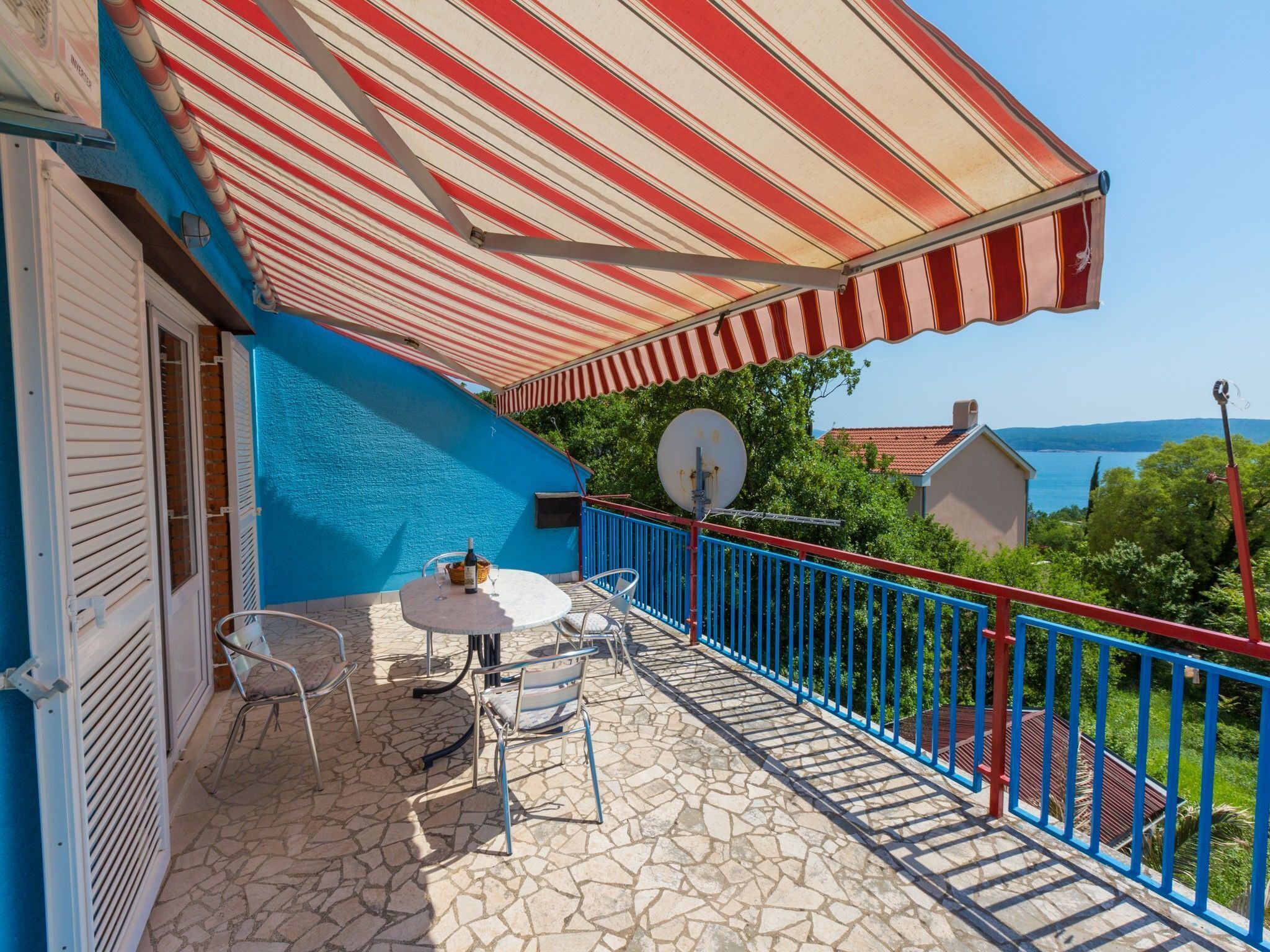 Un balcone con tenda a righe, un'antenna parabolica e un tavolo con sedie.