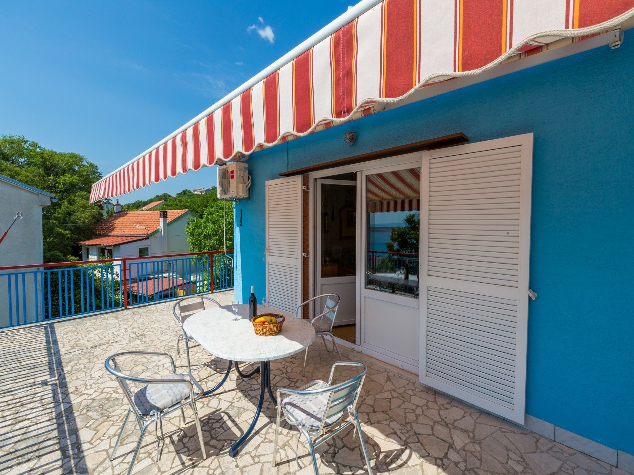 A blue building with a red and white striped awning, a white door, and a table with chairs outside.