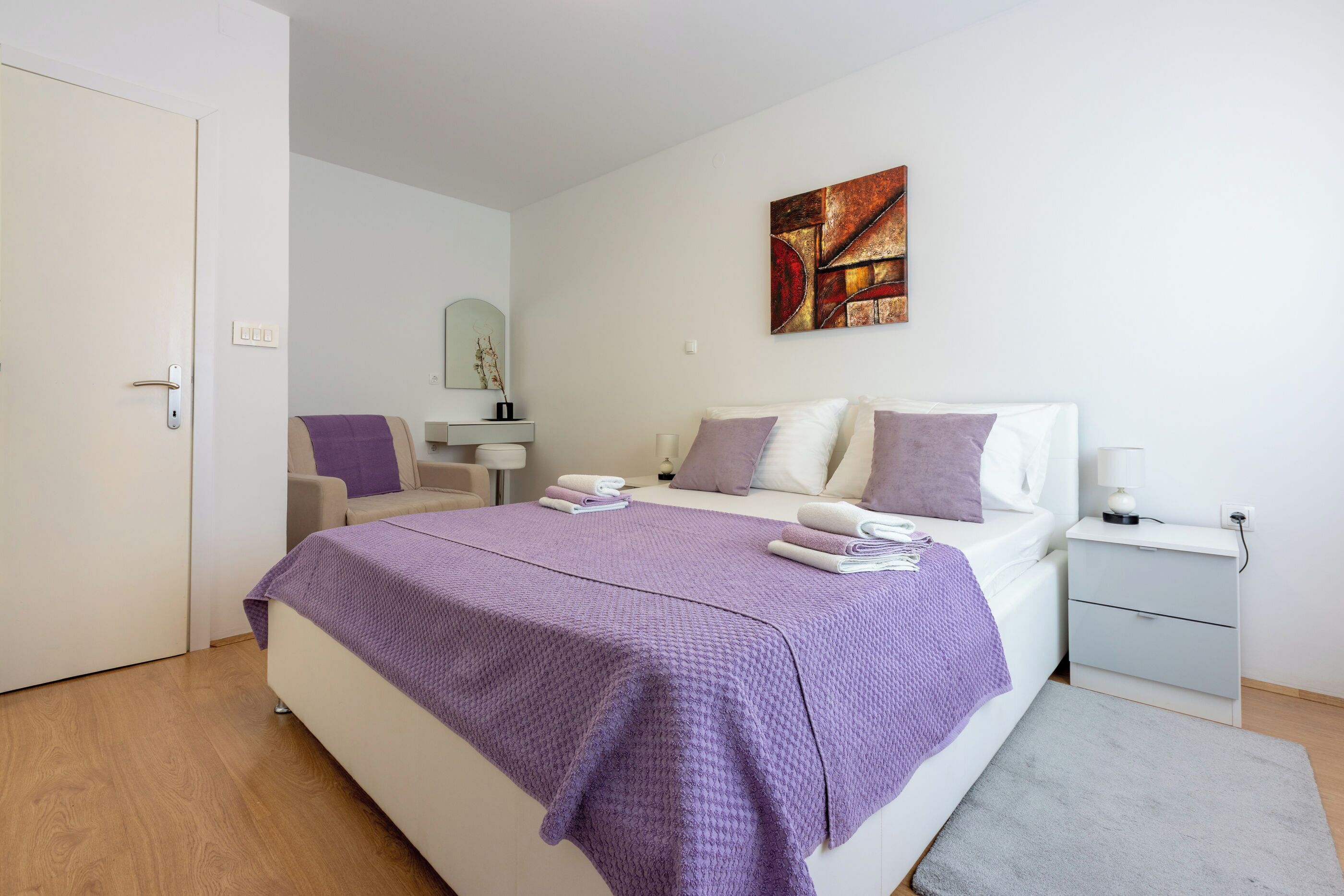 Een slaapkamer met een bed, nachtkastjes, een stoel en een schilderij aan de muur.