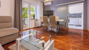 A modern living room with a glass coffee table, a sofa, and a dining area with chairs and a TV. - Apartment Villa Zdenka (Crikvenica)