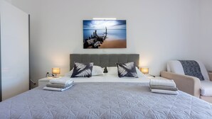 A neatly made bed with a quilted blanket, two pillows with a leaf pattern, a bedside table with a lamp, and a wall-mounted picture of a beach scene. - Apartment Villa Zdenka (Crikvenica)