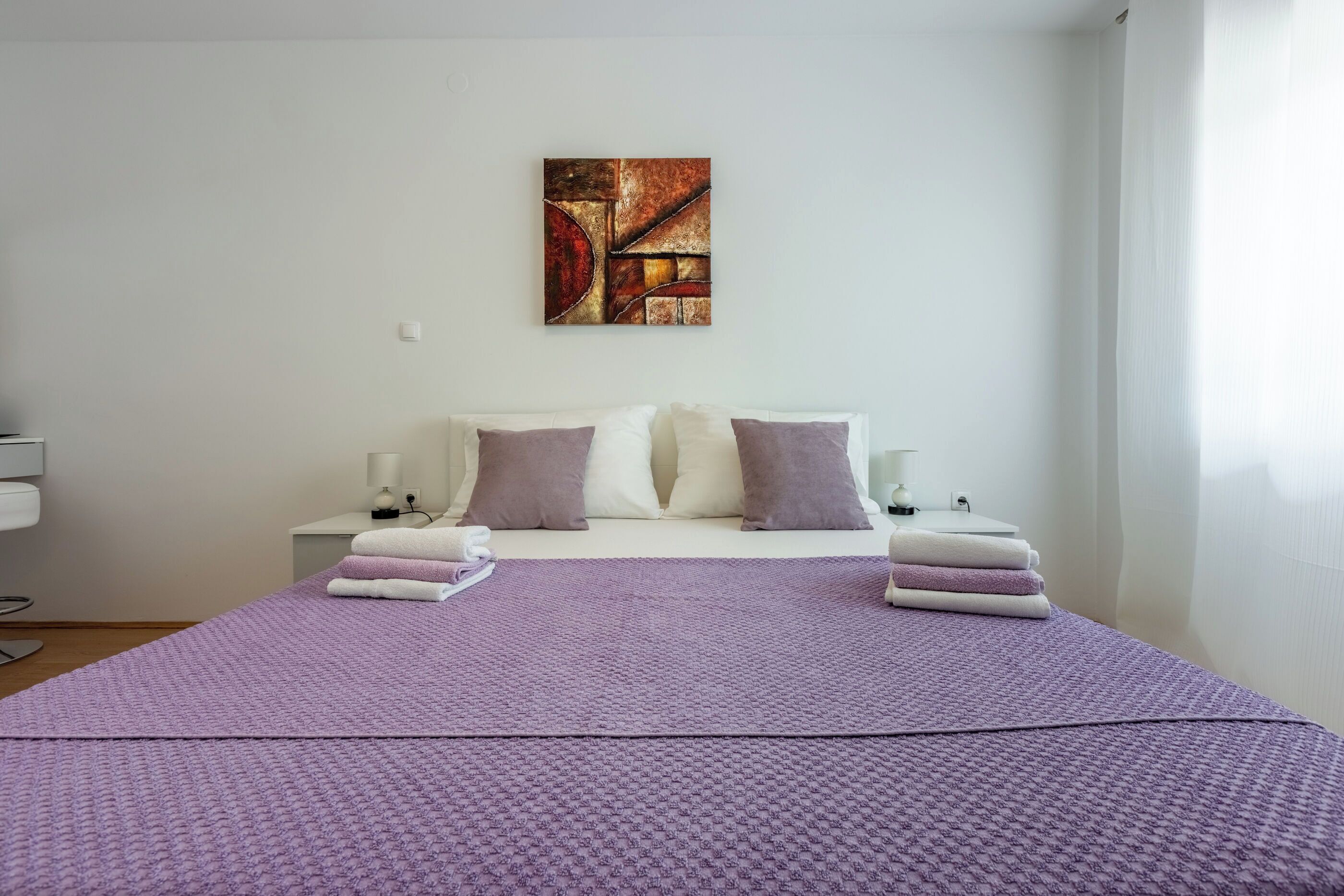 Un dormitorio moderno con una cama grande, dos mesitas de noche, un cuadro en la pared y una ventana.