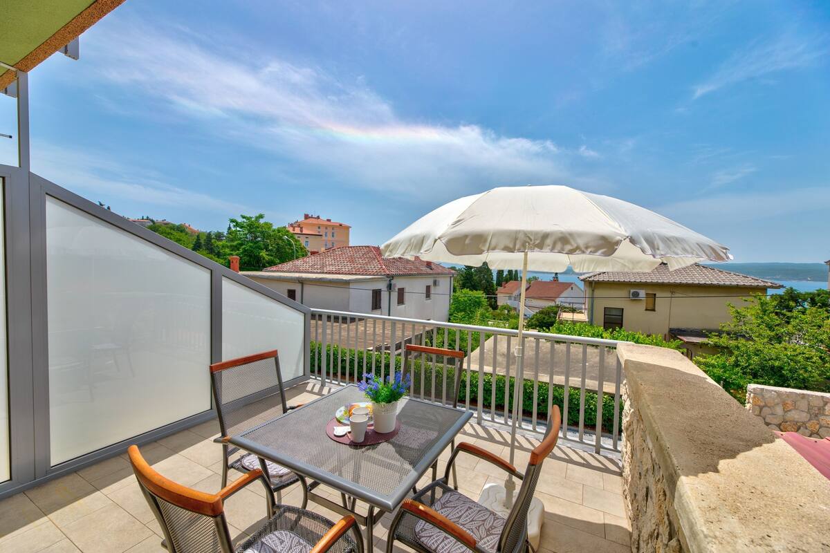 A balcony with a table, chairs, and a white umbrella.