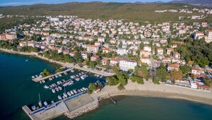 Vista aerea di una cittadina costiera con un porto turistico, edifici residenziali e una spiaggia.
