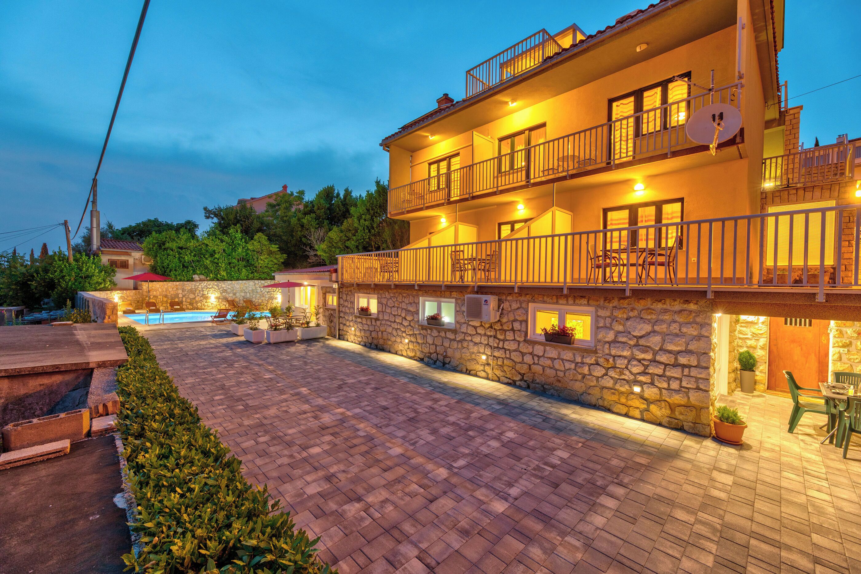 A two-story building with a stone facade, a swimming pool, and outdoor seating areas.