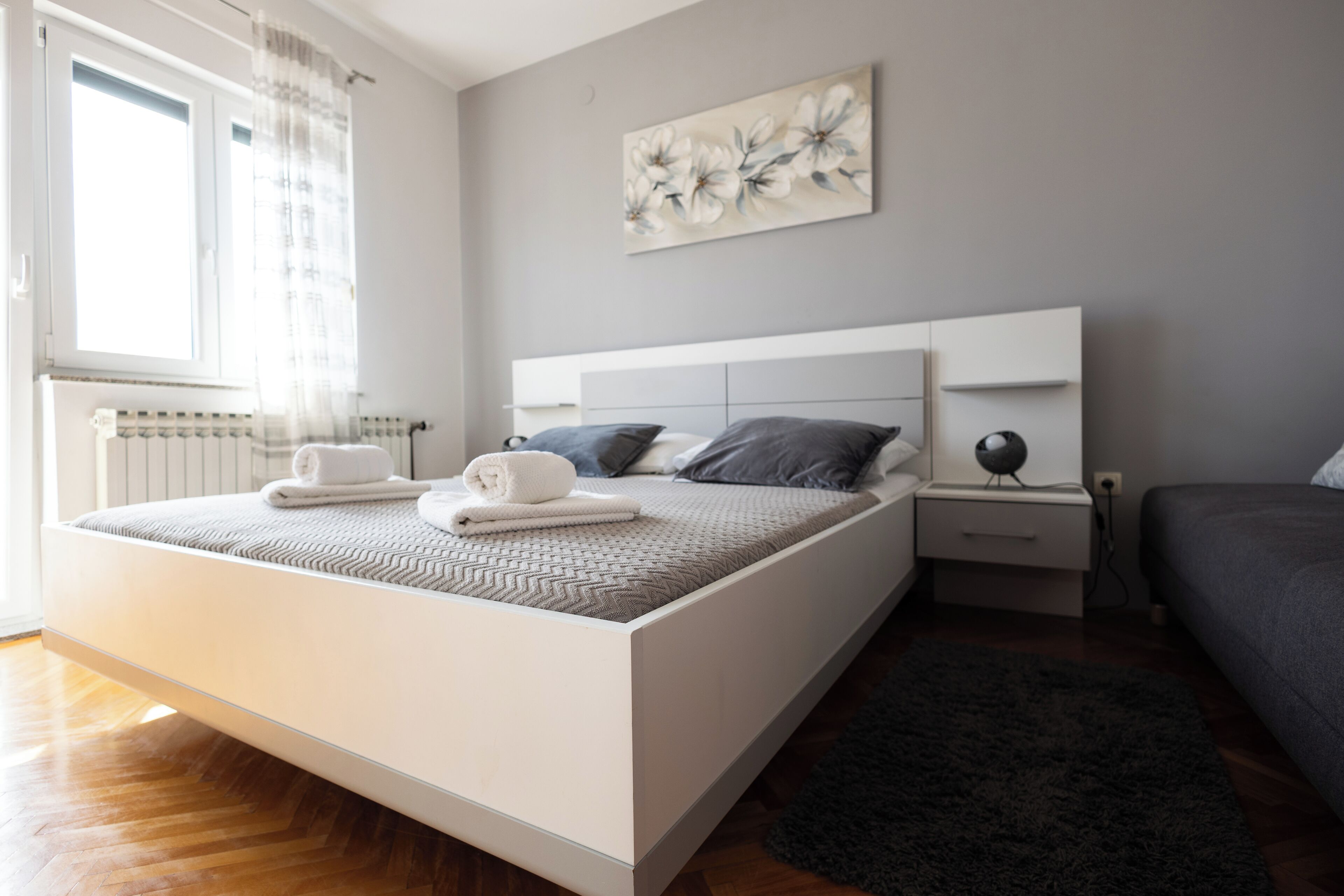 A modern bedroom with a large bed, bedside tables, a radiator, and a window with curtains.
