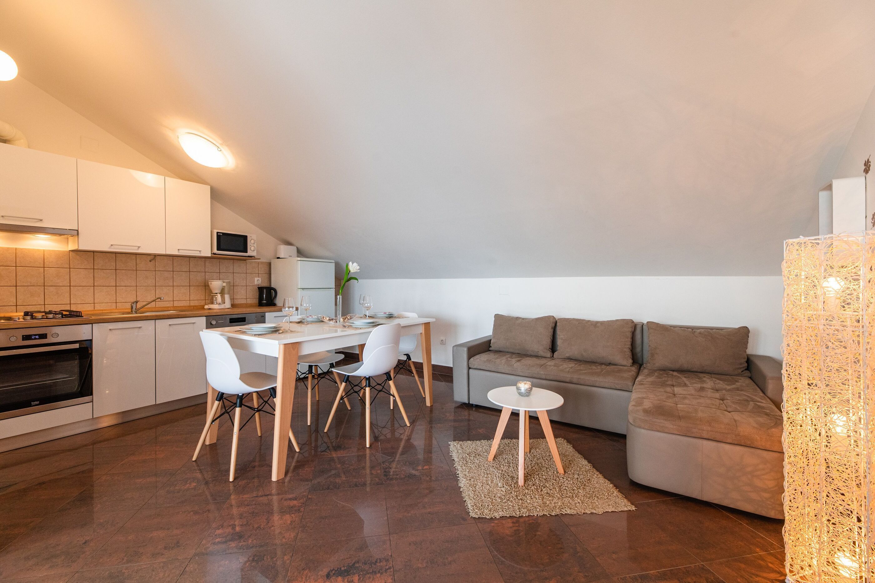 A modern kitchen with white cabinets, a dining area with white chairs, and a brown sofa.