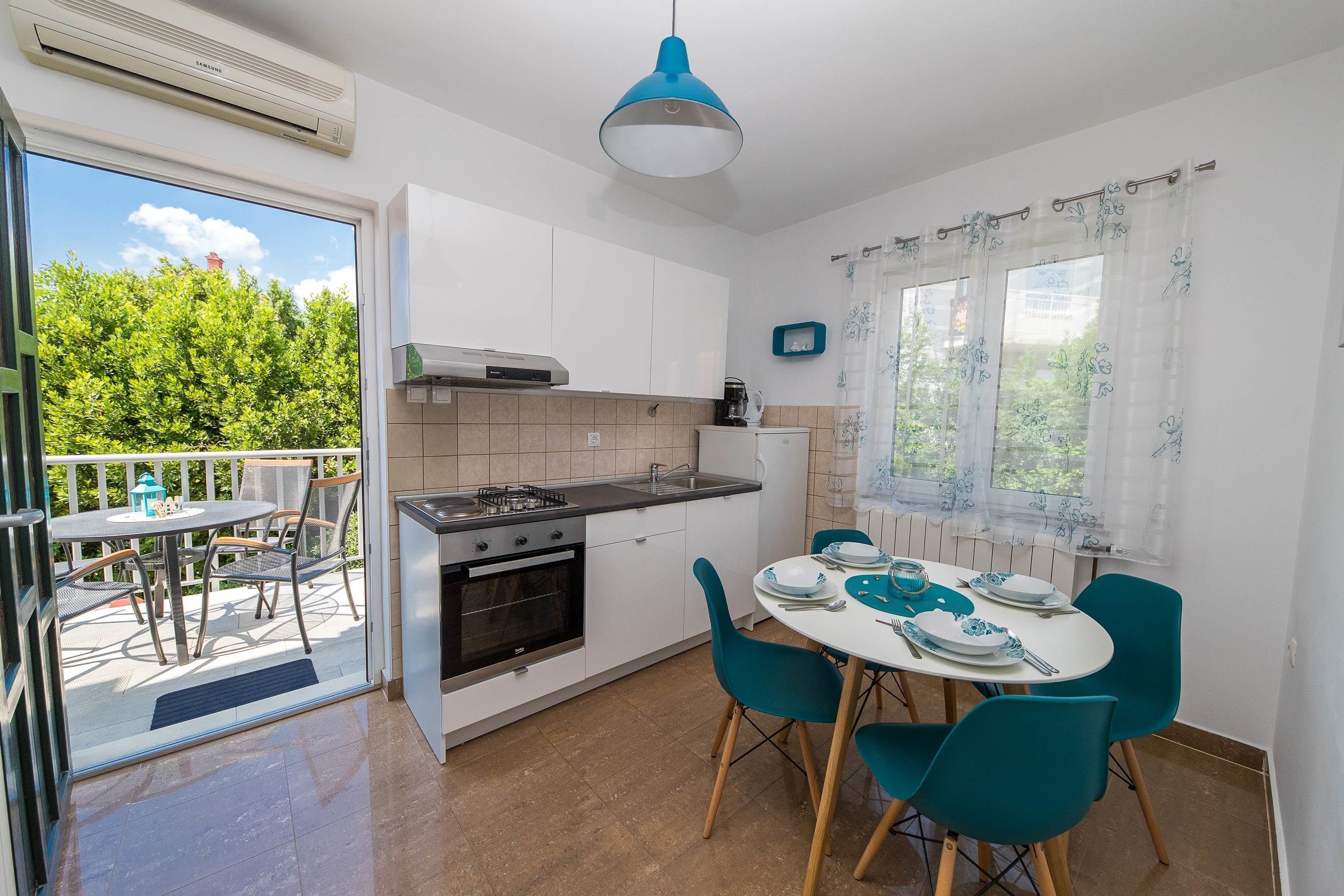 A modern kitchen with a gas stove, oven, and a dining area with teal chairs and a white table.
