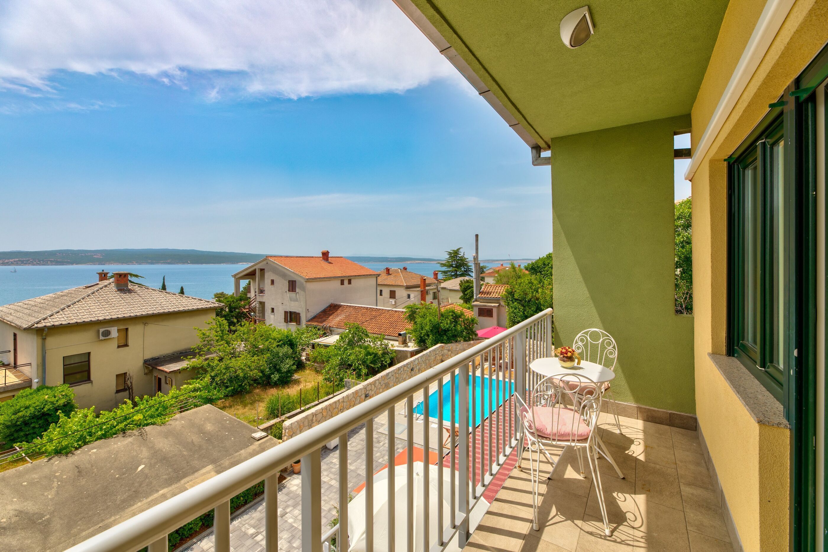 A balcony with a view of the sea, a swimming pool, and a table with chairs.