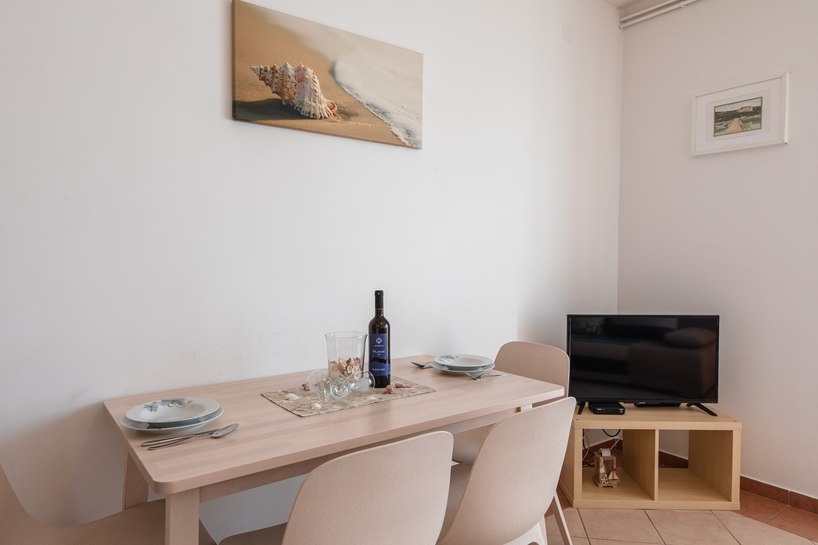 Een eethoek met een tafel gedekt voor twee personen, een televisie op een standaard en een lijst aan de muur.