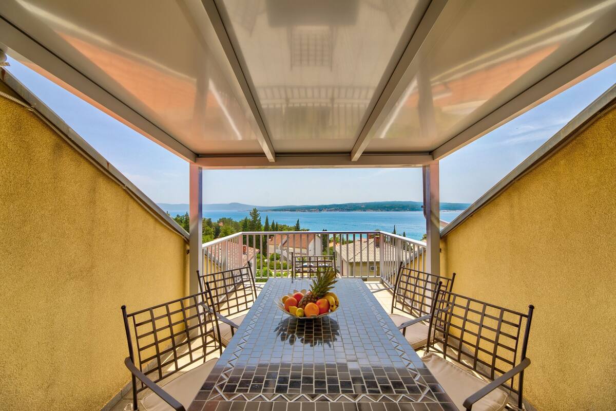 A balcony with a table, chairs, and a fruit bowl.