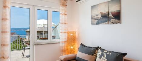 A living room with a sofa, a painting, and a view of the sea through a window.