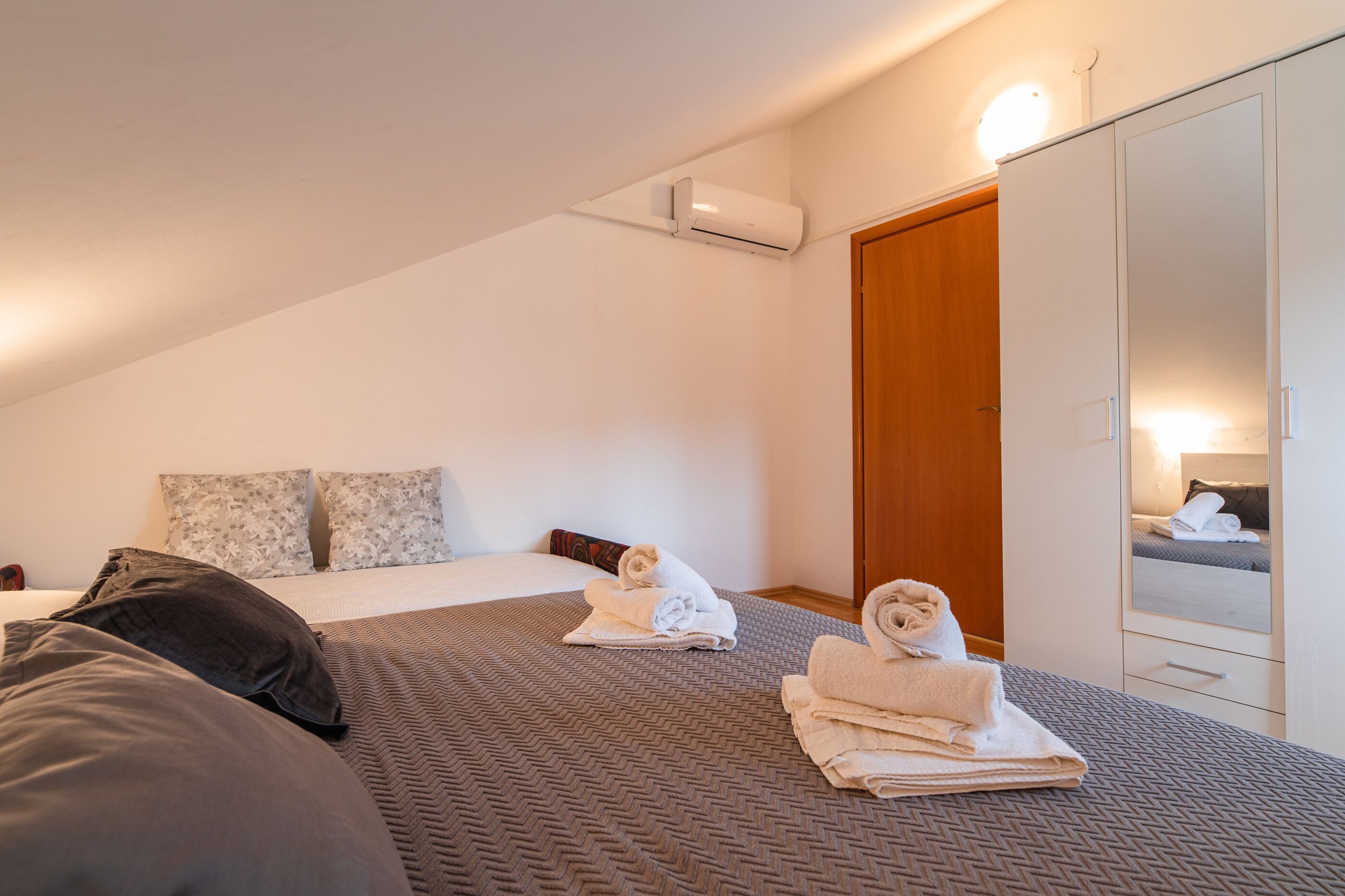 A bedroom with a bed, pillows, a bedside table, a mirror, and a wardrobe.