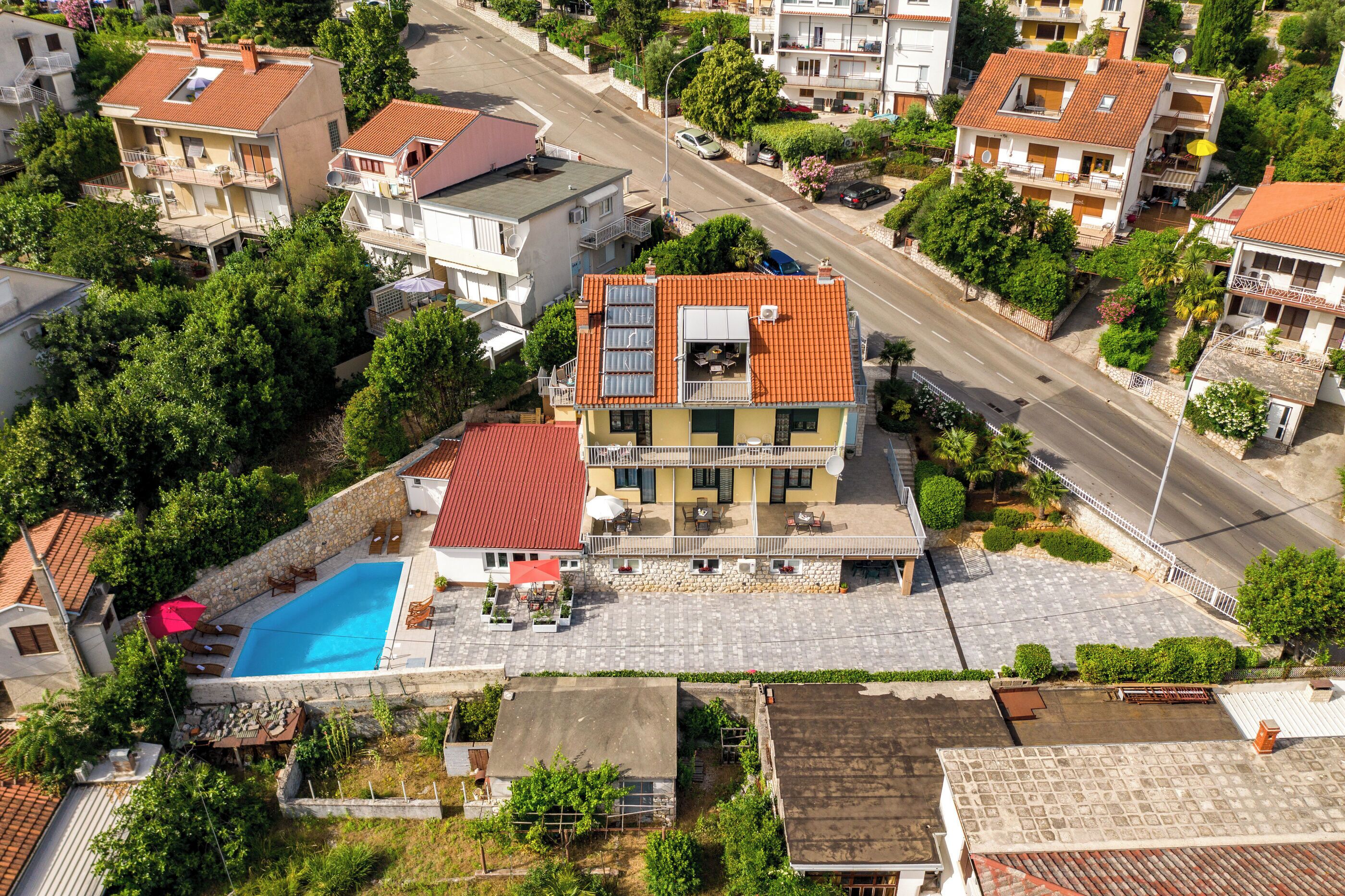 A multi-story residential building with a swimming pool, balconies, and a red-tiled roof.