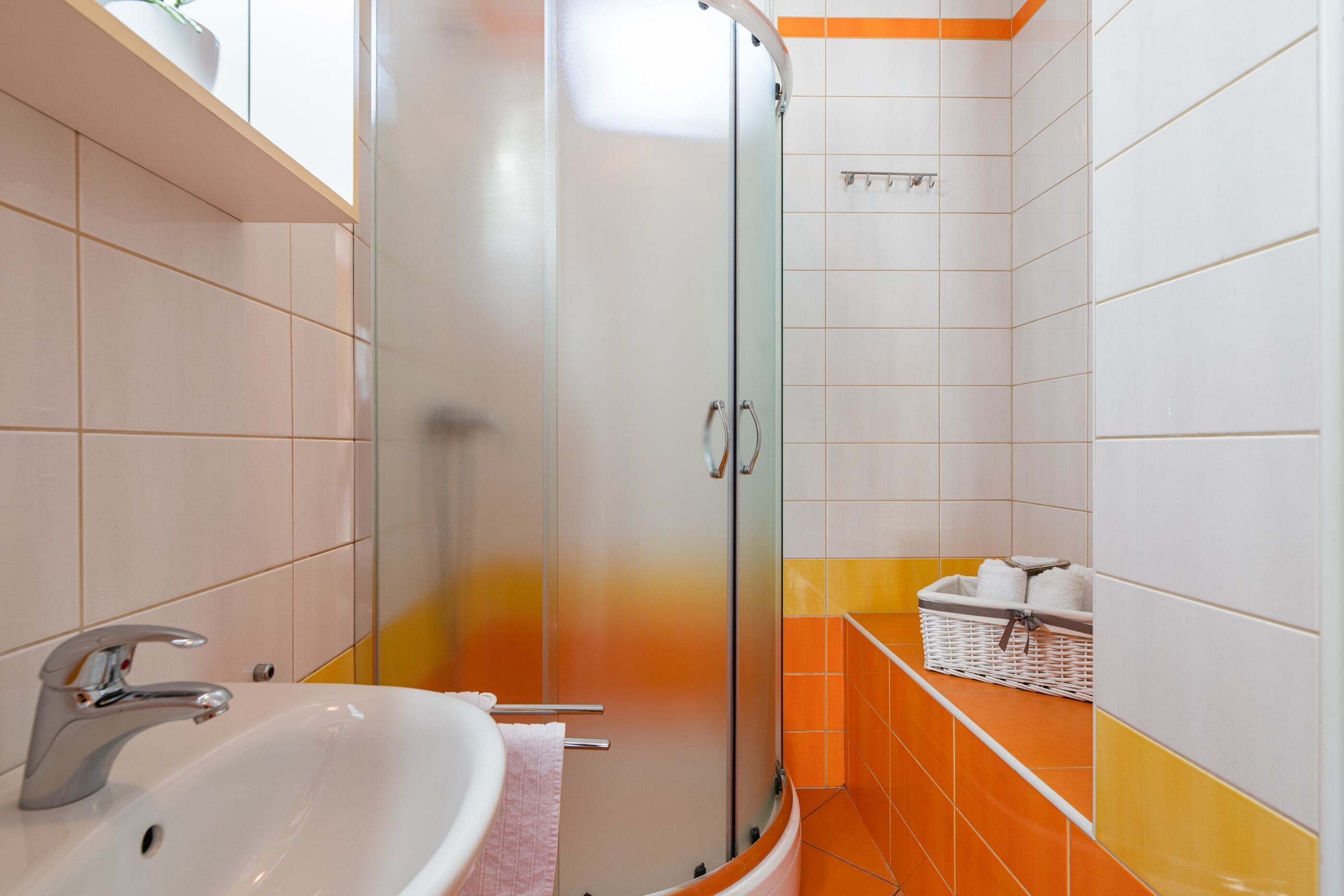 Un baño con ducha de vidrio, un lavamanos con toalla y una cesta de toallas en la pared.