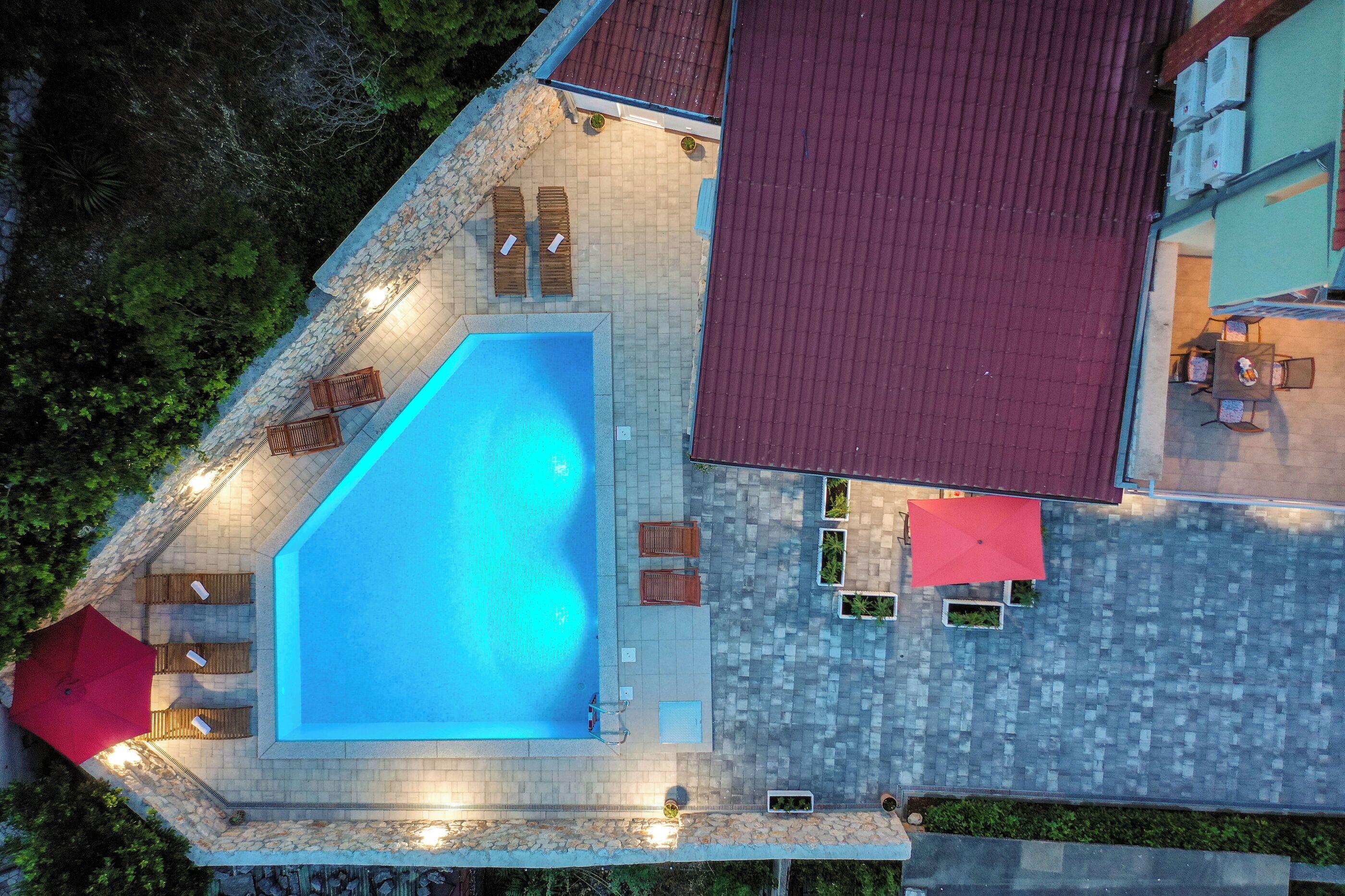 Vista aérea de un área de piscina con sillas de descanso, una sombrilla roja y un muro de piedra.
