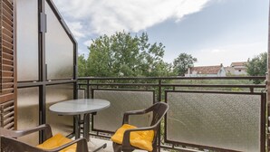 Un balcon avec deux chaises et une table, une rambarde en métal et une vue sur les arbres et les bâtiments.
