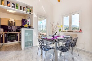 A modern kitchen with a built-in oven, a dining area with a glass table and black chairs, and a view of the outdoors through large windows. - Apartment Dario (Crikvenica)