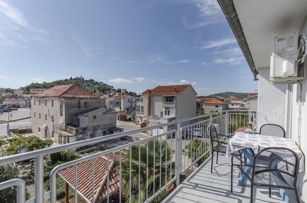 A balcony with a table and chairs, overlooking a residential area with buildings and a hill in the background.