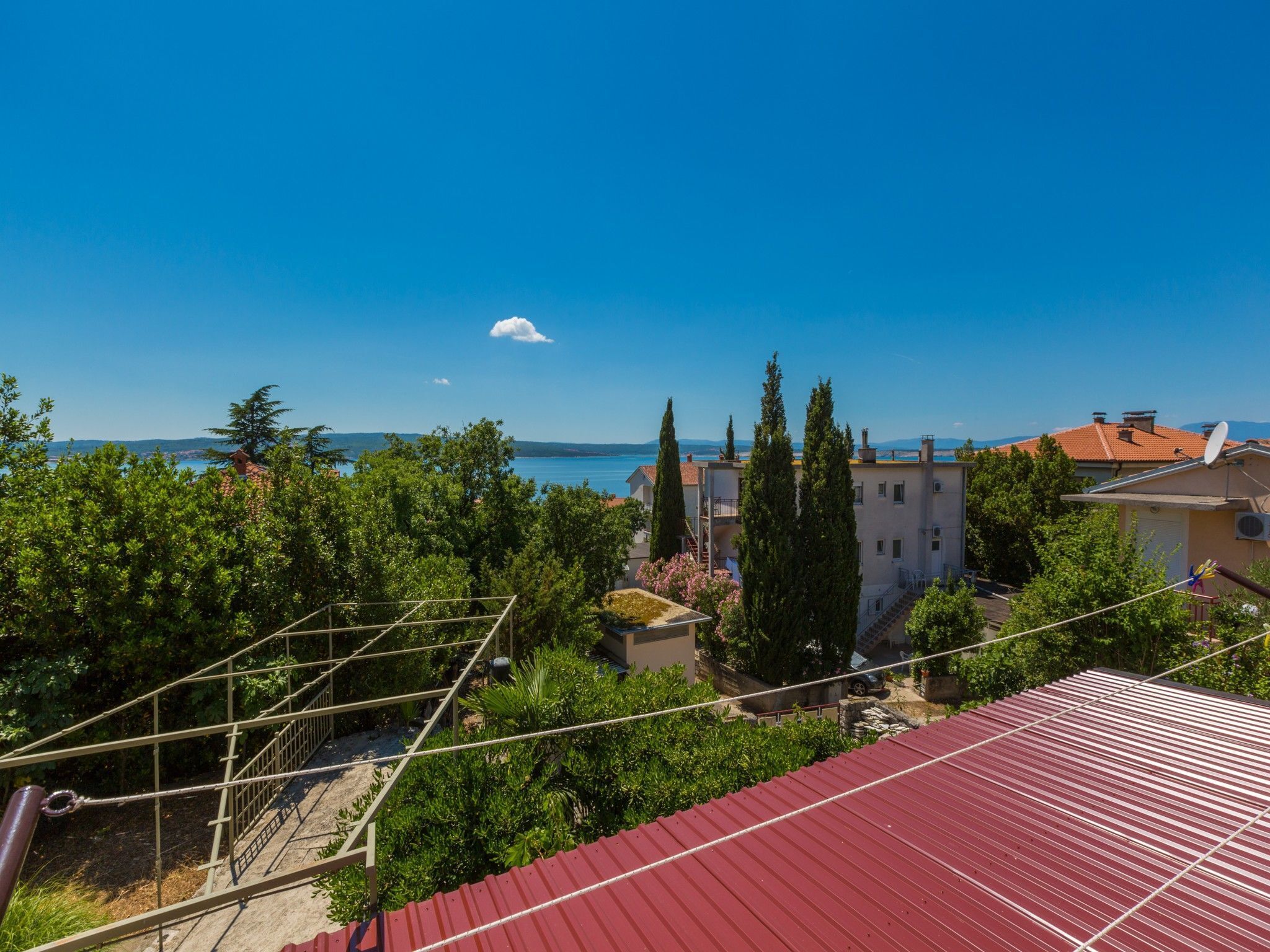 A residential area with a view of the sea, a red-roofed building, and a clear sky.