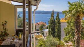 A balcony with a table set for breakfast, overlooking a coastal view with trees and a clear sky. - Apartments Miroslava (Crikvenica)