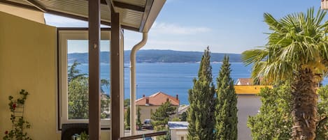 A balcony with a table set for breakfast, overlooking a coastal view with trees and a clear sky.