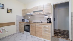 A modern kitchen with light wood cabinets, a built-in oven, microwave, and coffee maker. - Apartments Miroslava (Crikvenica)