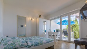 A bedroom with a bed, a desk, and a balcony with chairs and an umbrella. - Apartment Weiny (Crikvenica)