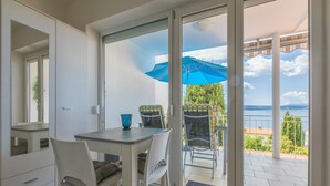 A dining area with a table and chairs, a blue umbrella, and a view of the sea through large glass doors. - Apartment Weiny (Crikvenica)