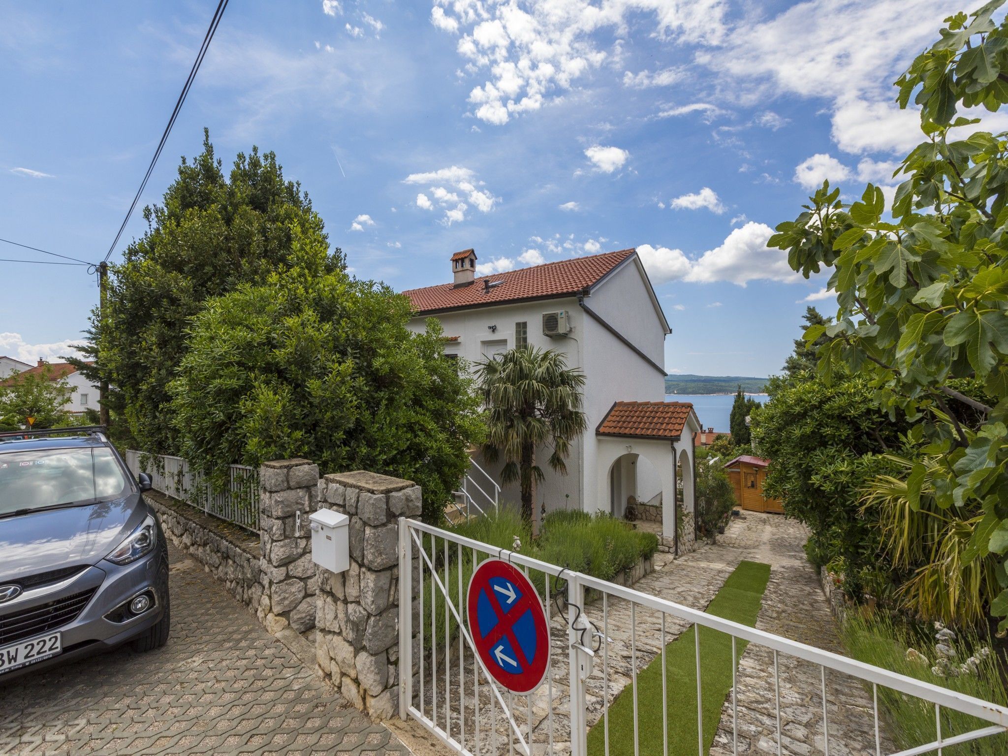 Un quartiere residenziale con una casa bianca, un muro in pietra e un cartello che indica divieto di parcheggio.