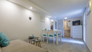 A compact living space with a sofa, a small dining table with chairs, a kitchenette, and a bathroom visible through an open door. - Apartment Weiny (Crikvenica)