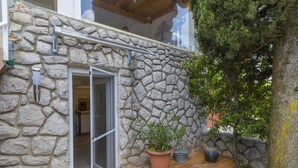 A stone exterior wall with a wooden deck, a potted plant, and a tree. - Apartment Weiny (Crikvenica)