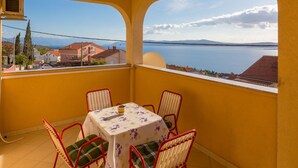 A balcony with a table and chairs, overlooking a body of water and distant mountains. - Apartments Roko (Crikvenica)