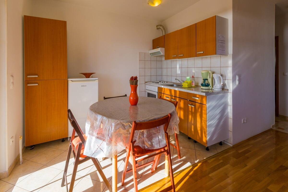 A compact kitchen with wooden cabinets, a refrigerator, a sink, and a table with chairs.