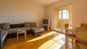 A living room with a sofa, a small table, a television, and a dining area with chairs. - Apartments Roko (Crikvenica)