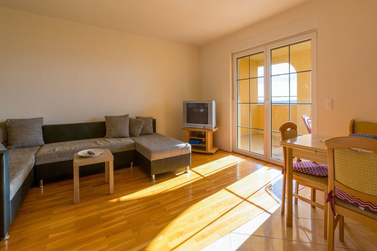 A living room with a sofa, a small table, a television, and a dining area with chairs.