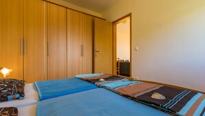 A bedroom with a large wardrobe, a bed with blue bedding, and a nightstand with a lamp. - Apartments Roko (Crikvenica)
