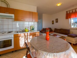 A compact kitchen with wooden cabinets, a stove, and a dining table with a lace tablecloth.