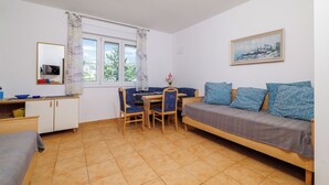 A compact room with a bed, a desk with a chair, a small table, a TV, and a window with curtains. - Apartment Regan (Crikvenica)