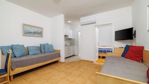 A room with a sofa, a bed, a TV, and a kitchen area. - Apartment Regan (Crikvenica)