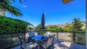 A terrace with a table and chairs, overlooking a body of water and a town in the distance. - Apartment Regan (Crikvenica)