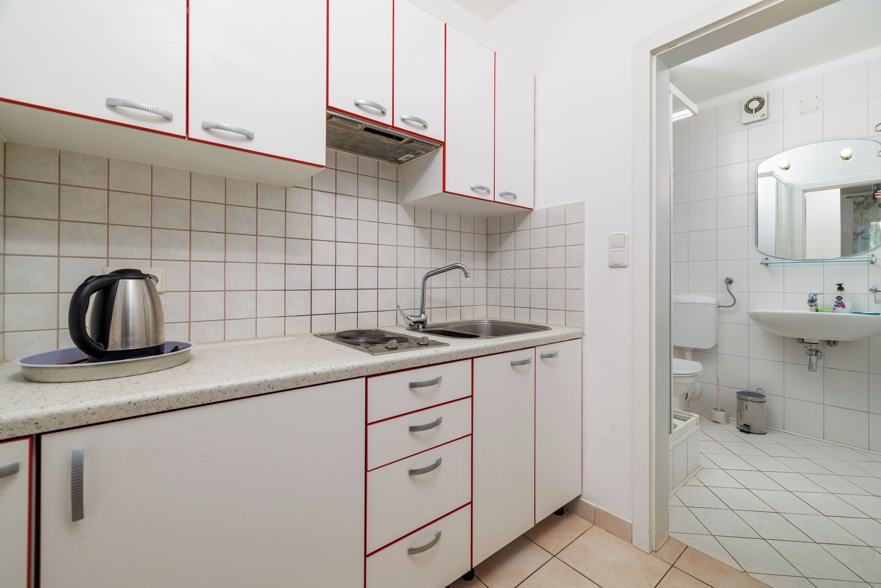 A kitchen with white cabinets, a stainless steel kettle, a sink, and a tiled backsplash.